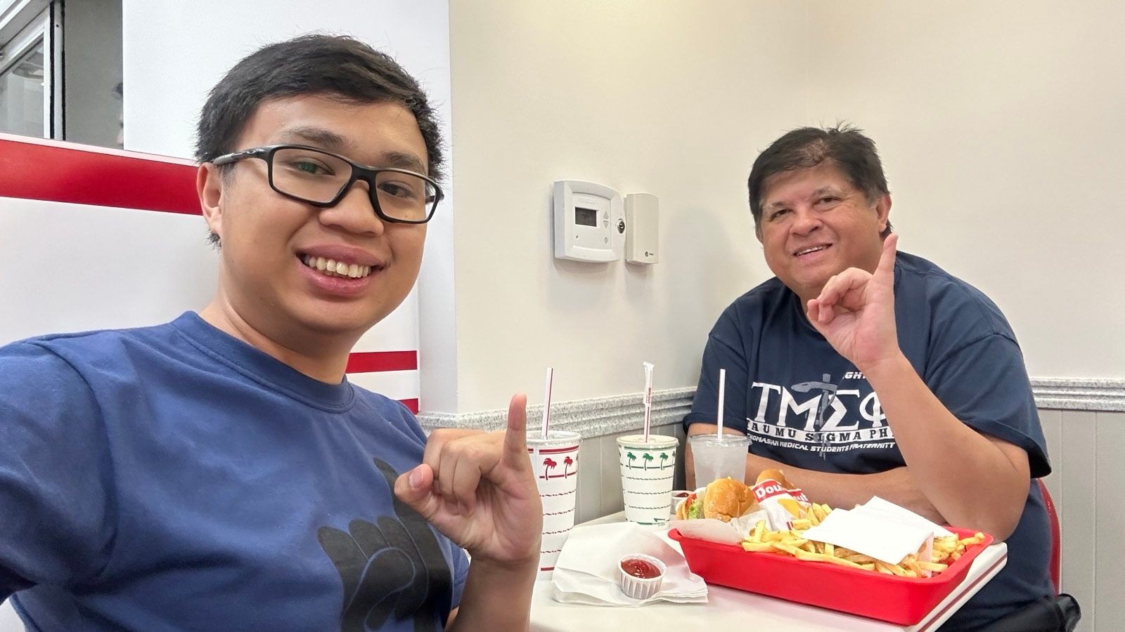 Two people smiling at a fast food restaurant table with fries, burgers, and drinks.